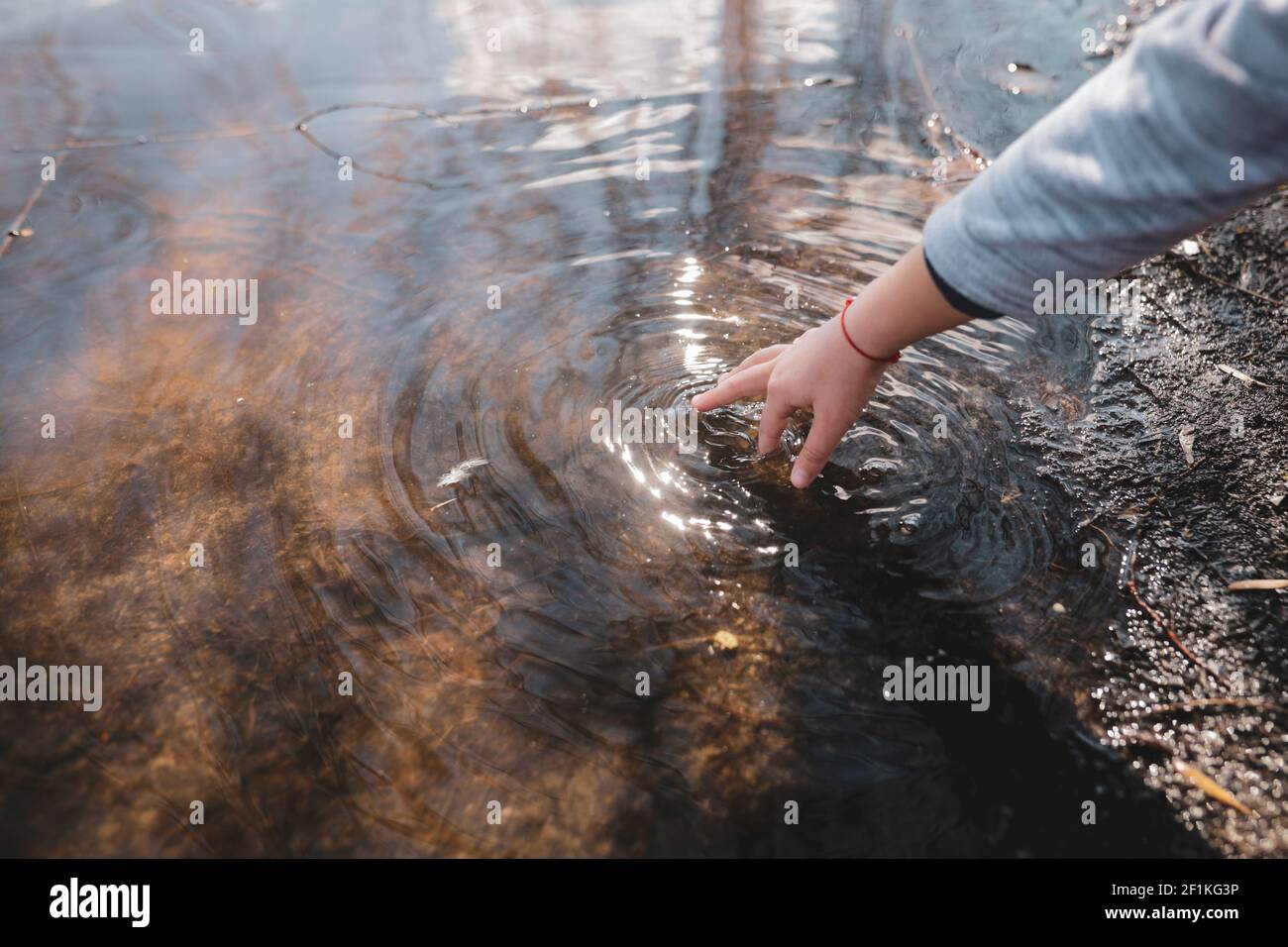Shallow depth of field (selective focus) details with the hand of a young girl playing with her hand in the shallow water of a lake. Stock Photo