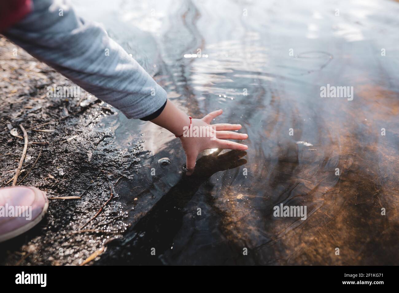 Shallow depth of field (selective focus) details with the hand of a young girl playing with her hand in the shallow water of a lake. Stock Photo