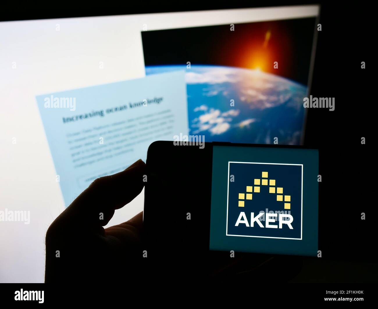 Person holding cellphone with business logo of Norwegian investment company Aker ASA on screen in front of web page. Focus on phone display. Stock Photo