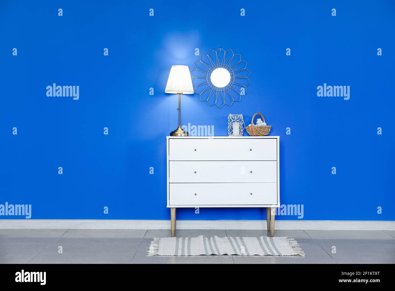 Chest of drawers with glowing lamp near color wall in room Stock Photo