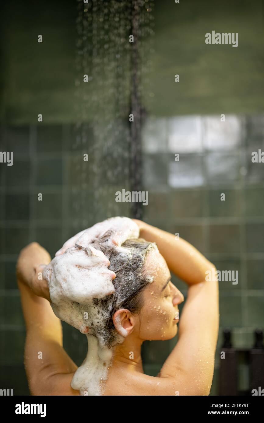 Woman staying back in shower apply shampoo with water dripping. Taking