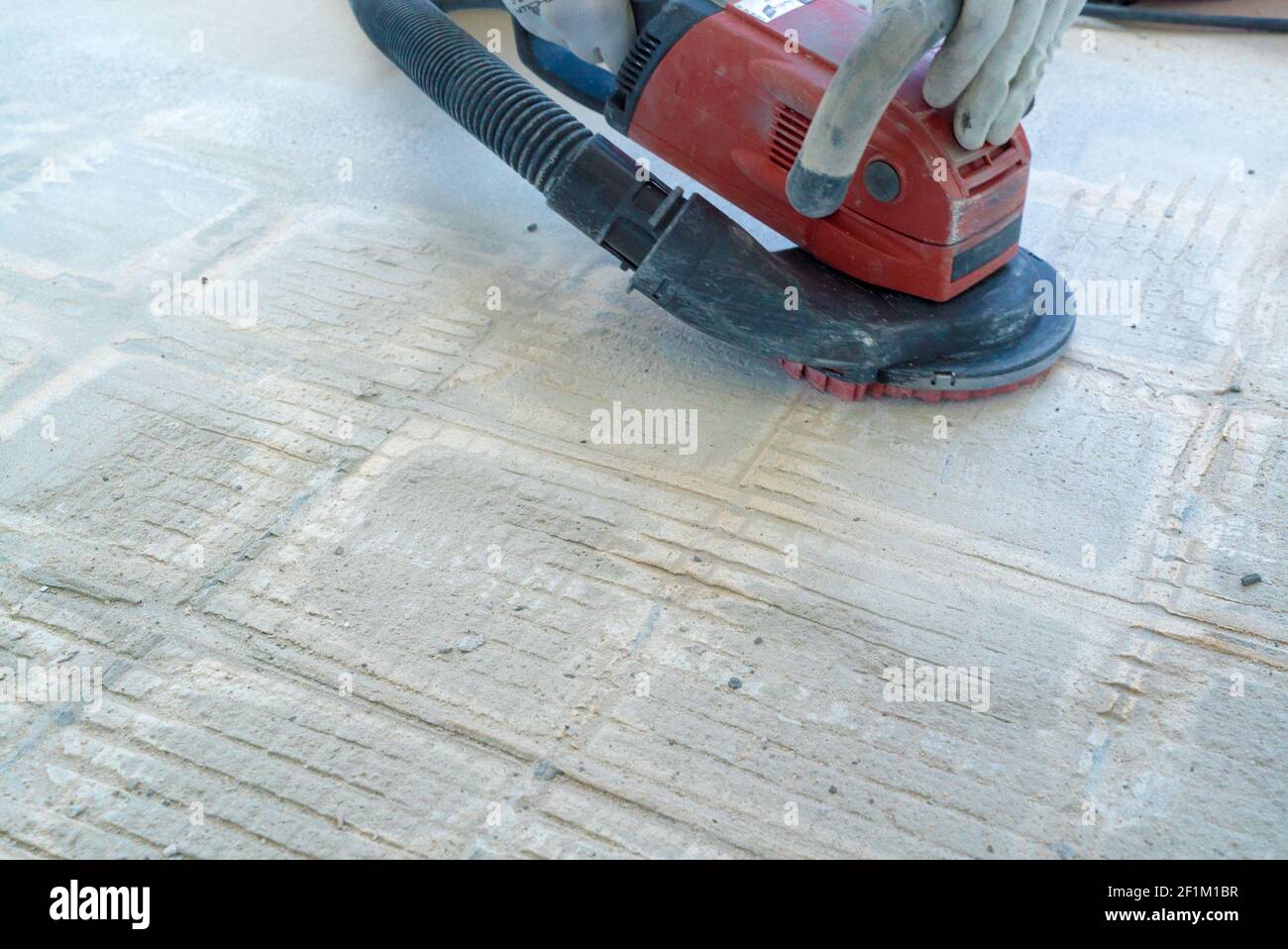 Construction worker uses a concrete grinder for removing tile glue and resin during renovation