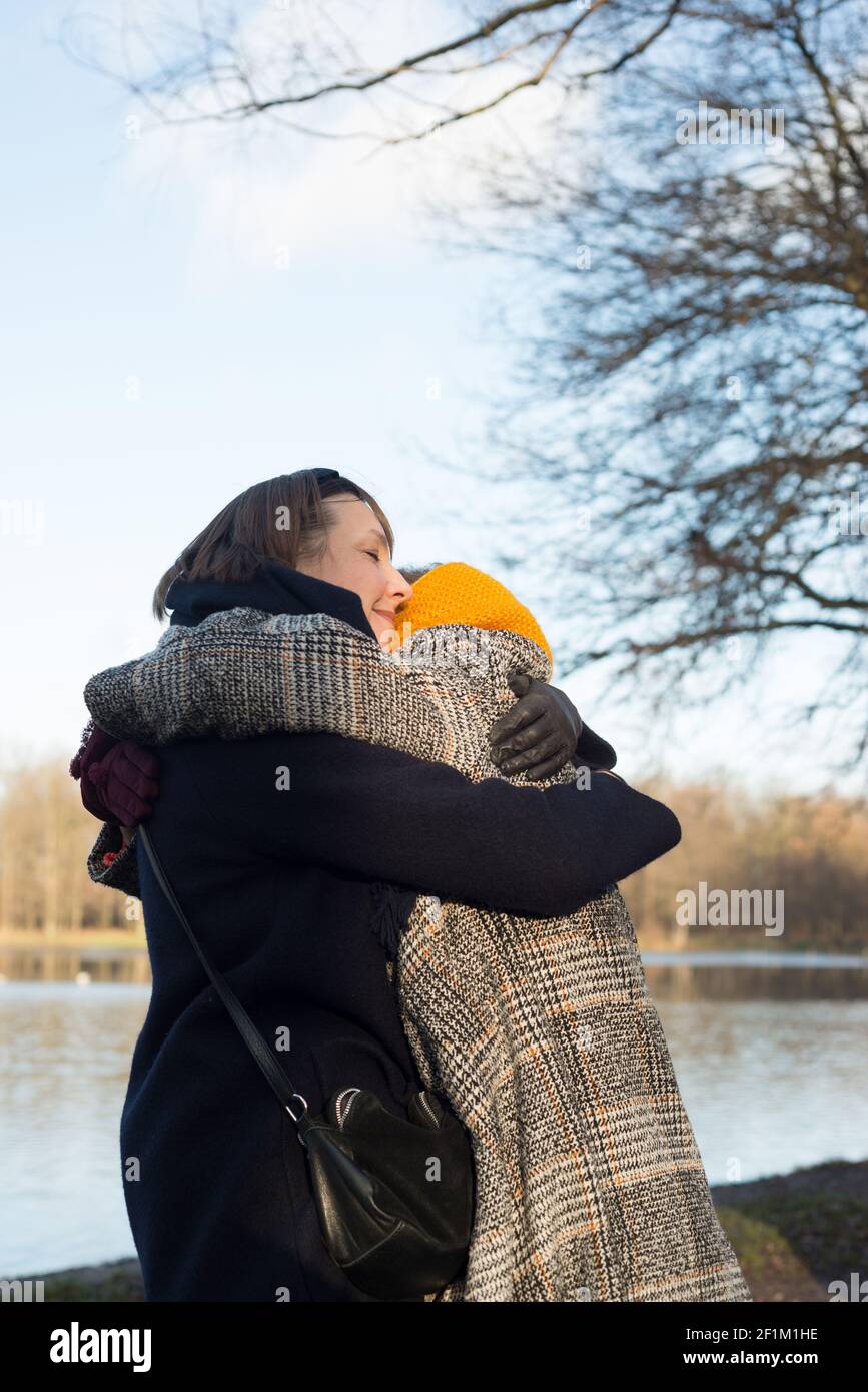 Two women in a coat hugging in nature Stock Photo - Alamy