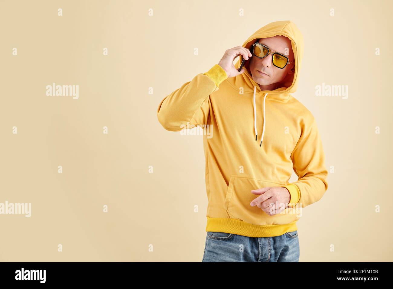 Studio portrait of man in yellow hoodie and sunglasses talking on phone
