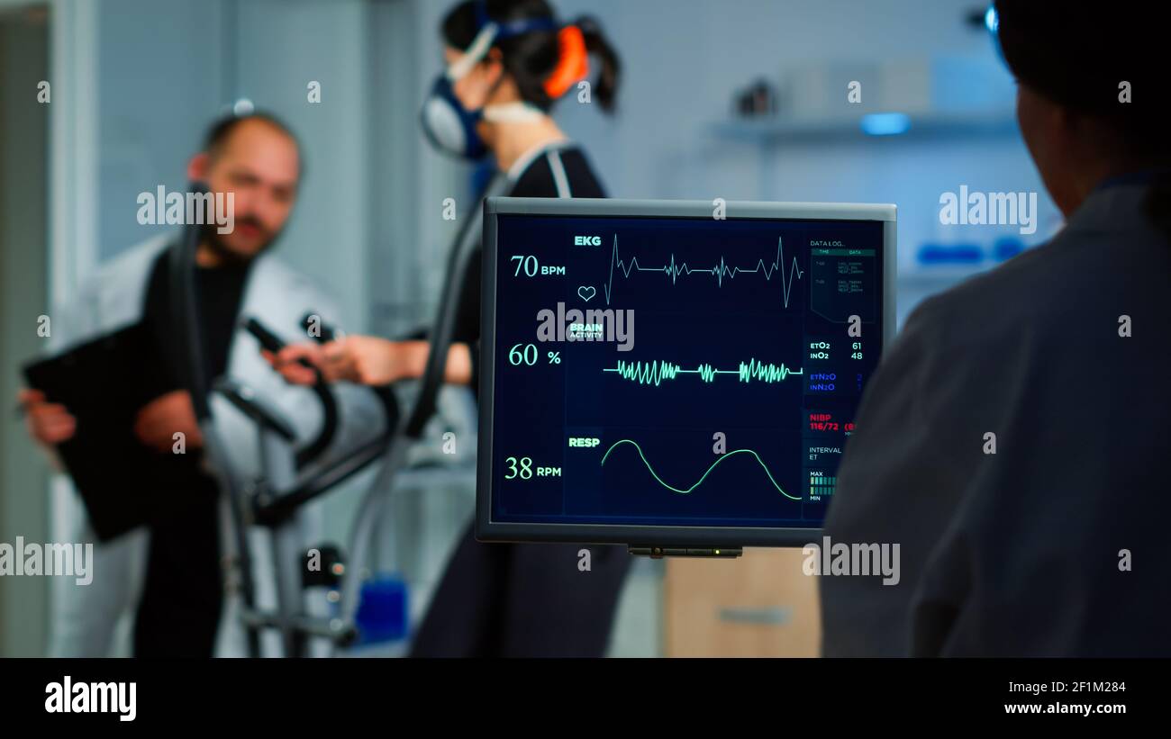 Medical researcher examining EKG image showing on monitor while with mask running on