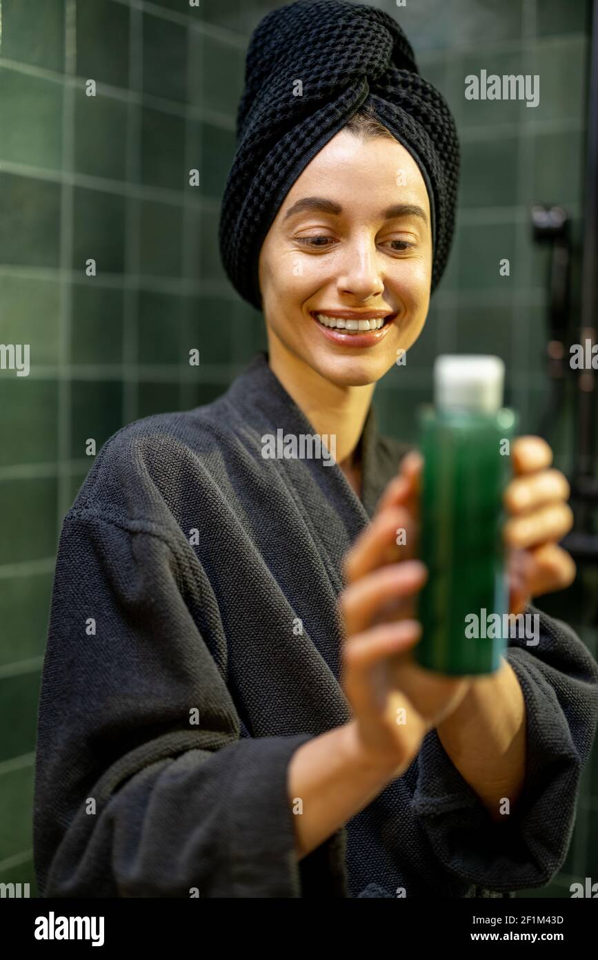 Woman after shower holding and looking on a bottle with green shampoo