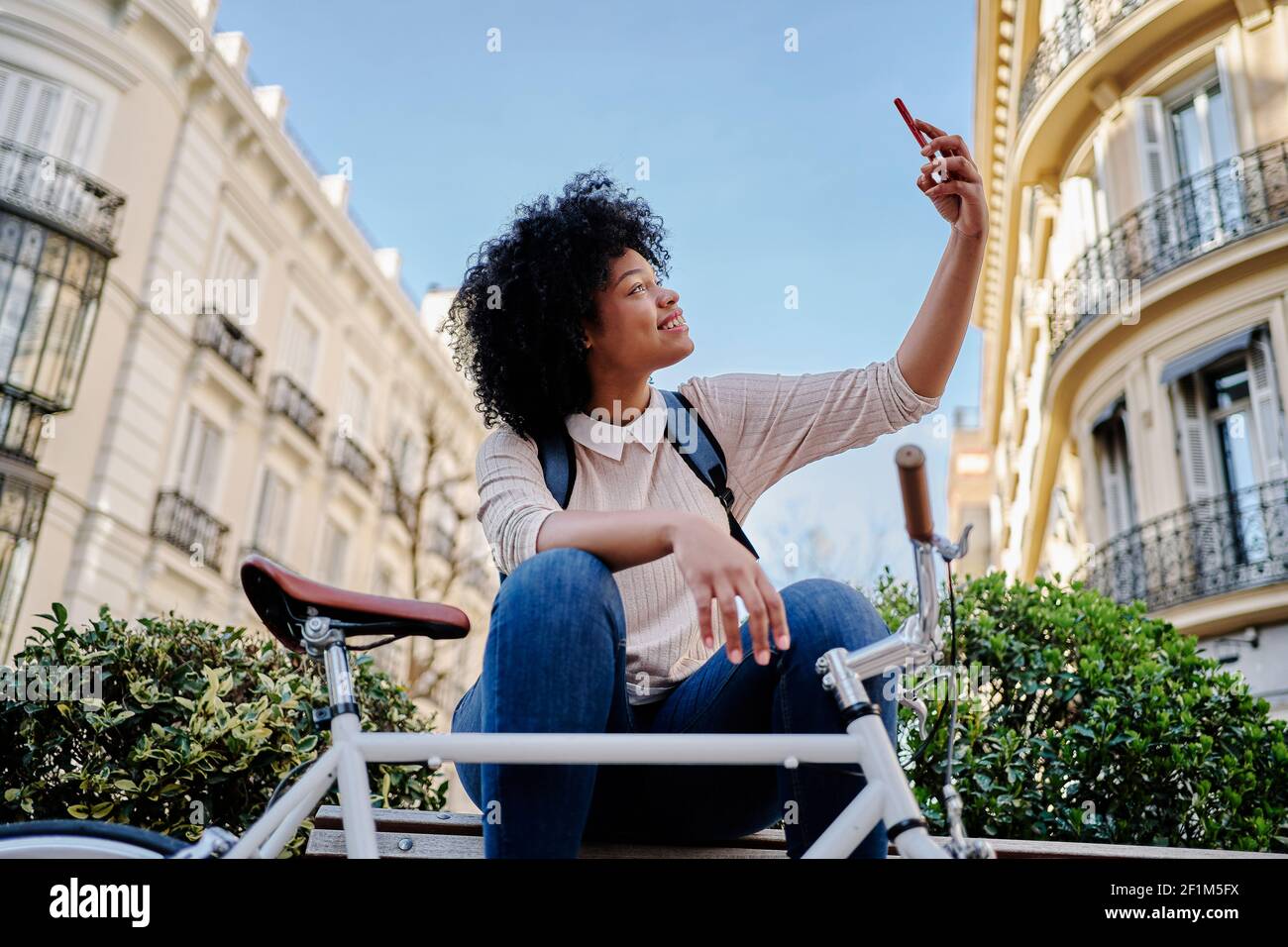 African American woman taking a self-portrait with her smart phone. Sitting on a bench with her bicycle. High quality photo Stock Photo