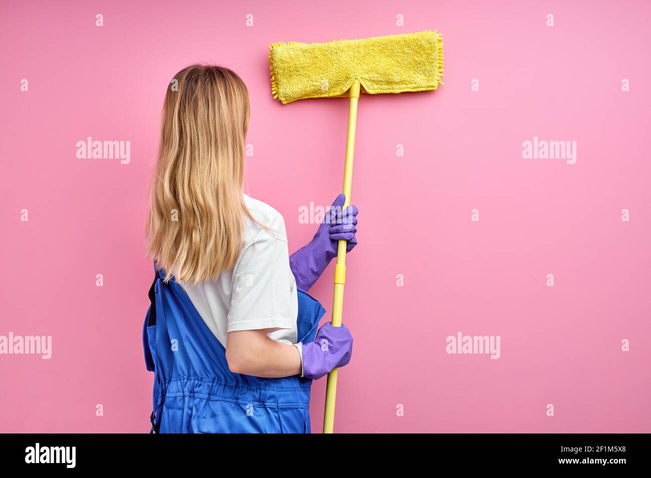 woman removes cobwebs from walls using mop rear view on young