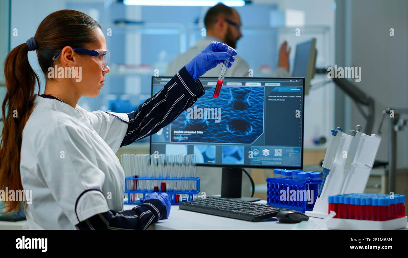 Scientist doctor looking at blood sample and typing on computer while ...
