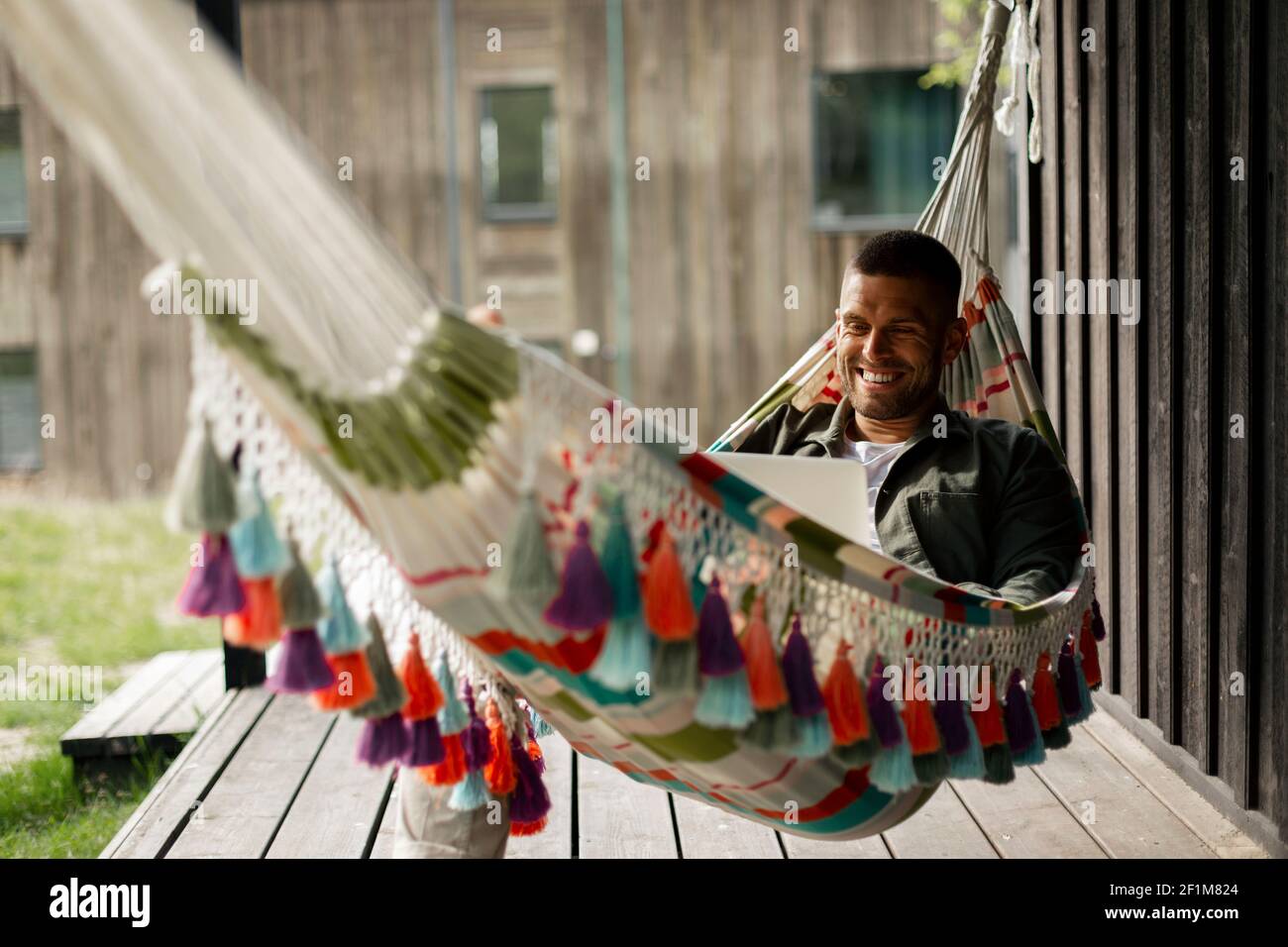 Smiling man using laptop while relaxing on hammock Stock Photo