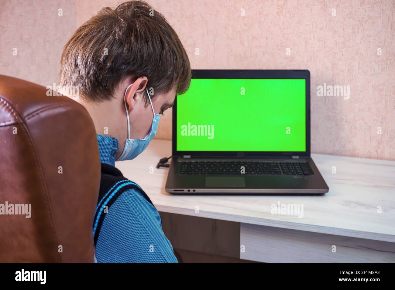 Man in a medical face mask sleeps at the workplace near a laptop with a green screen Stock Photo