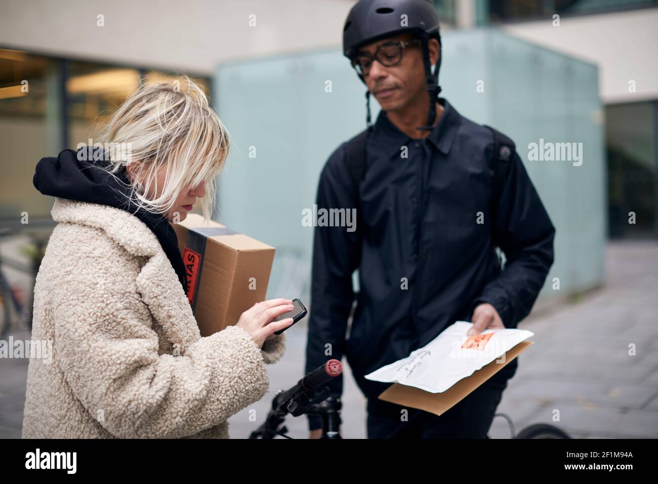Bicycle courier taking sign from female customer while delivering package Stock Photo