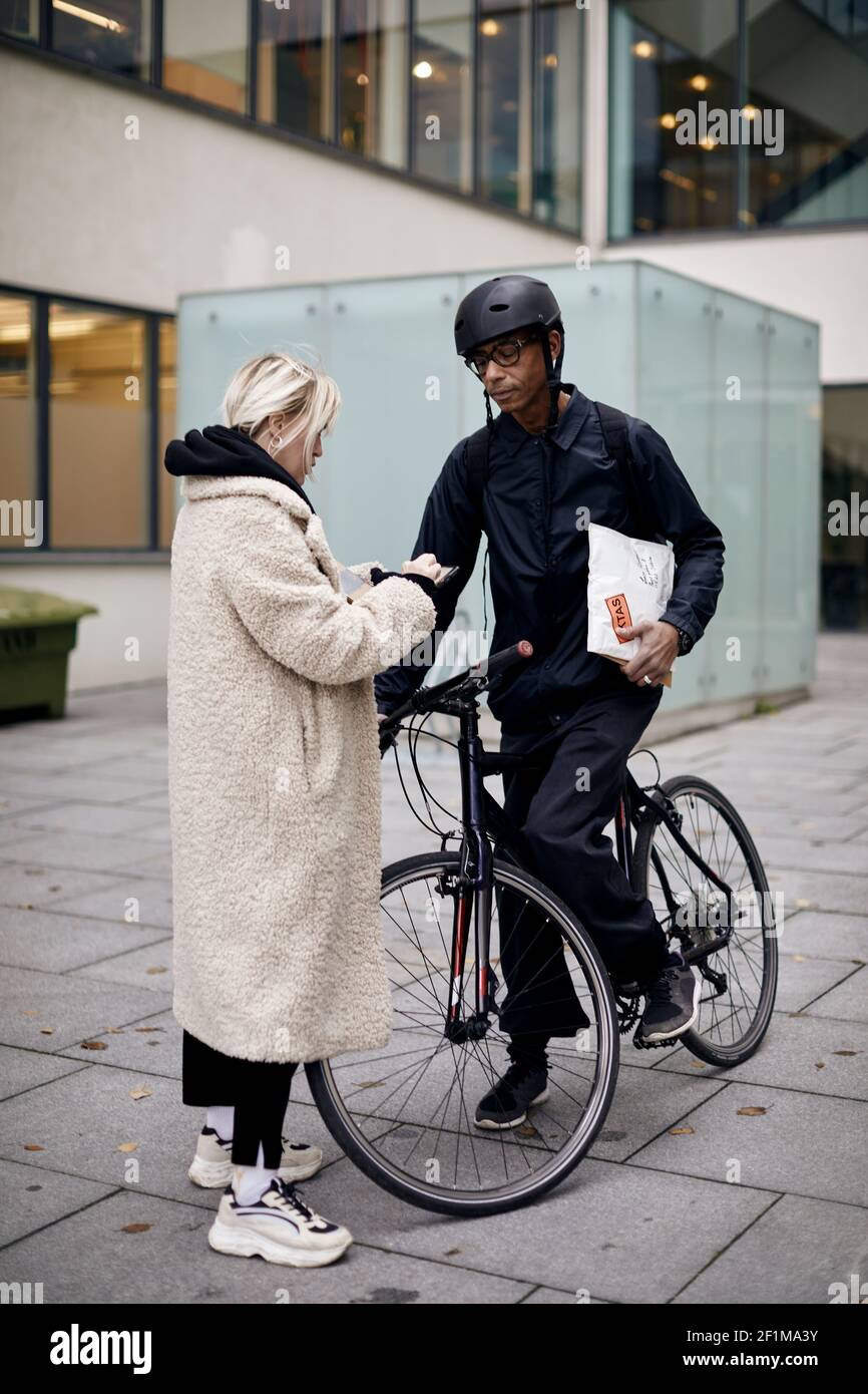 Bicycle courier taking sign from female customer while delivering package Stock Photo