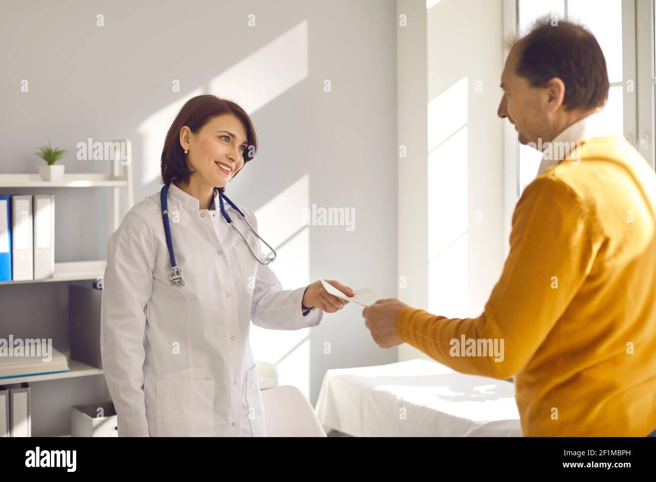 Female doctor giving medical prescription or certificate to middle aged patient Stock Photo