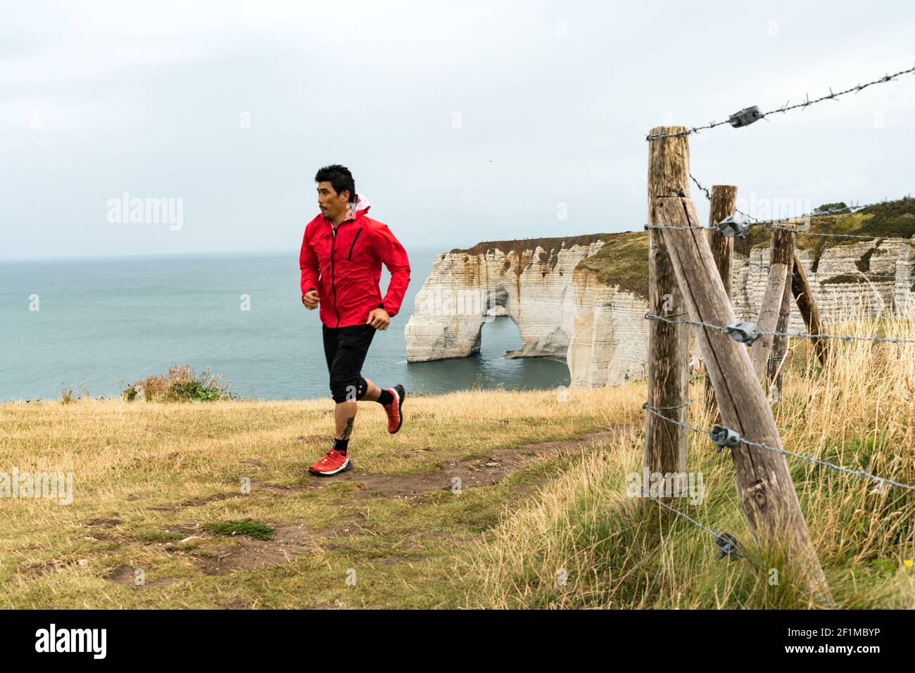 Asian man trail runner jogging on the Normandy coast along the Falaise de Etretat cliffs above the v Stock Photo