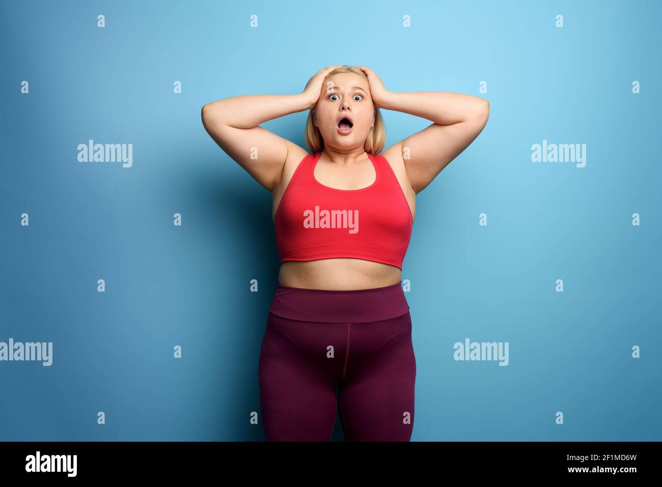 Fat girl in fitness suite wants to start a diet but has some. Cyan background Stock Photo