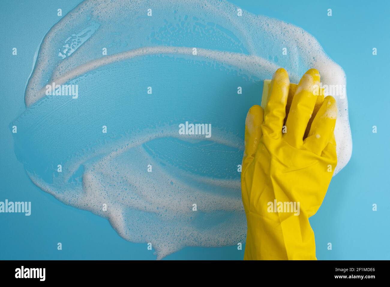 Female hand in protective yellow glove, sponge and foam on blue background. House cleaning concept. Top view. Copy space Stock Photo