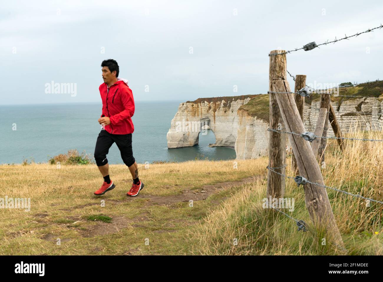 Asian man trail runner jogging on the Normandy coast along the Falaise de Etretat cliffs above the v Stock Photo