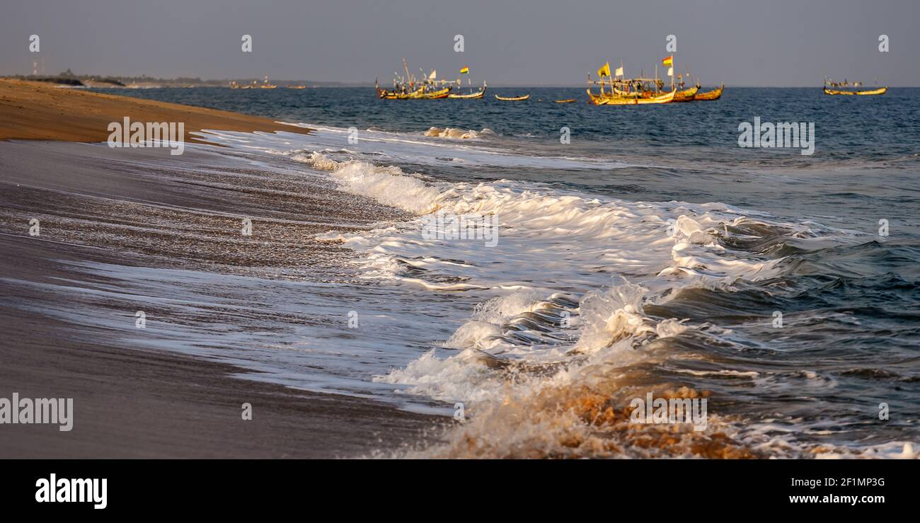 Sunset over Ghana's coast keta with foaming waves and fishing boats in the background Stock Photo