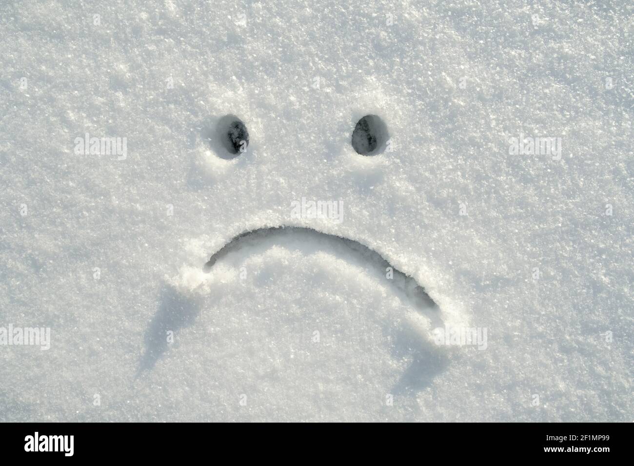 Sad smiley face drawn in the snow on a sunny winter day. Copy space. Negative emotions.  Stock Photo