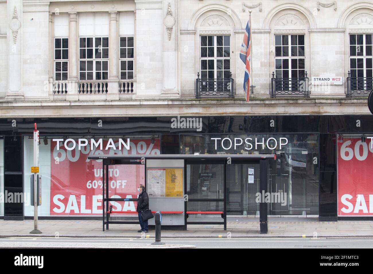 Closed shops in London, Topshop and Topman branch with bus stop in foreground with man wearing PPE mask, Strand, London ex subsidiary of the Arcadia Group went into administration in late 2020. The brand was sold to ASOS  in February 2021 Stock Photo