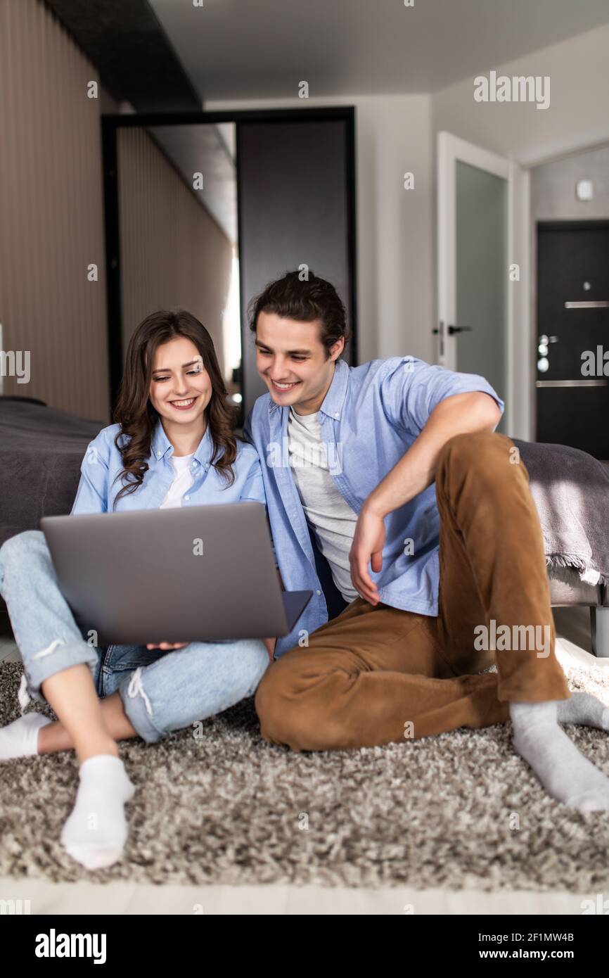 Lovely young couple sitting on the floor in the bedroom and looking at ...