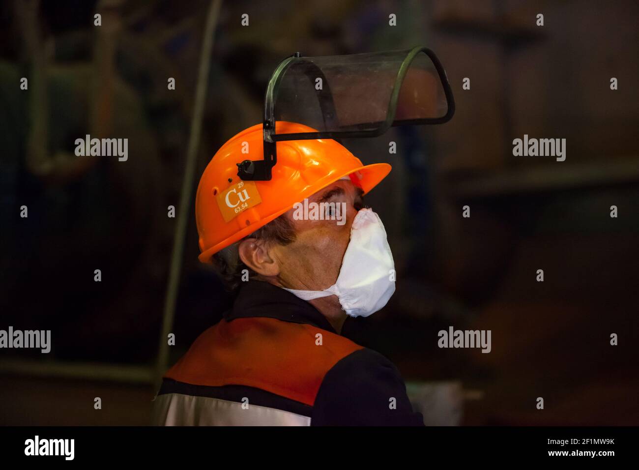 Copper metallurgy smelter plant. Metallurgist worker in orange hardhat, respirator and protective mask. Copper sign on helmet. Kazzinc company. Stock Photo