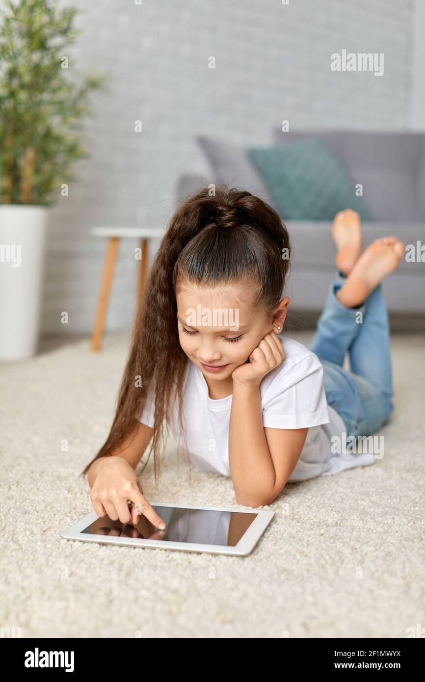 cute happy little child girl lying on the carpet and using digital ...
