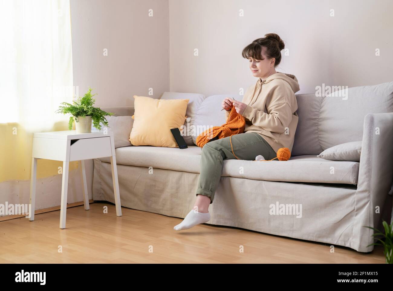 Young woman knitting on sofa at home Stock Photo