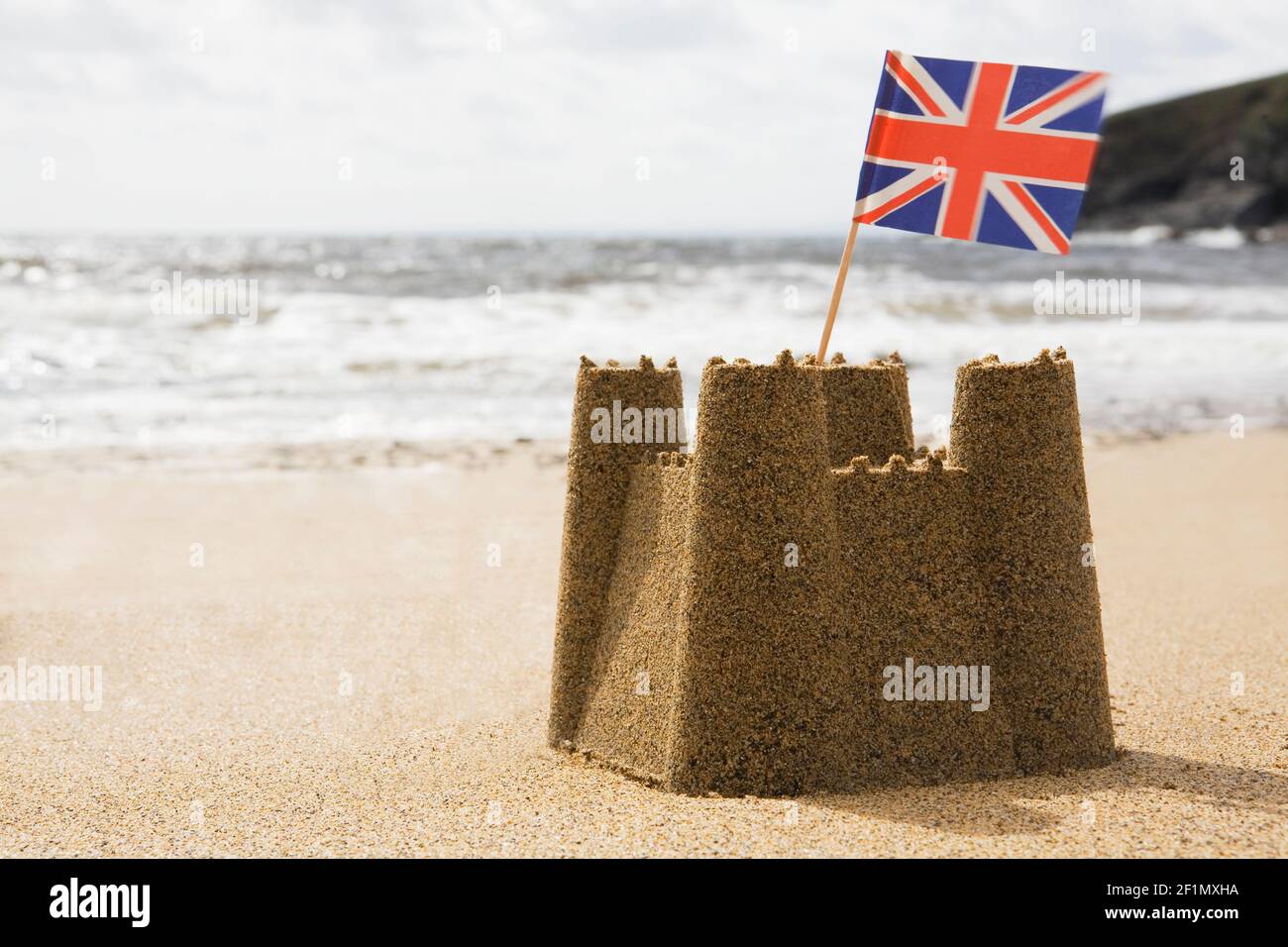 Sandcastle On Empty British Beach With UK Union Jack Flag Flying Stock Photo