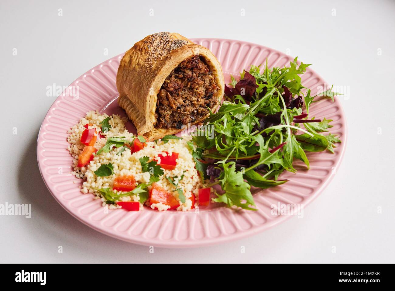 Vegan Meal On Plate With Savoury Roll Filled With Chickpea Lentil And Mushroom Next To Couscous And Salad On White Background Stock Photo