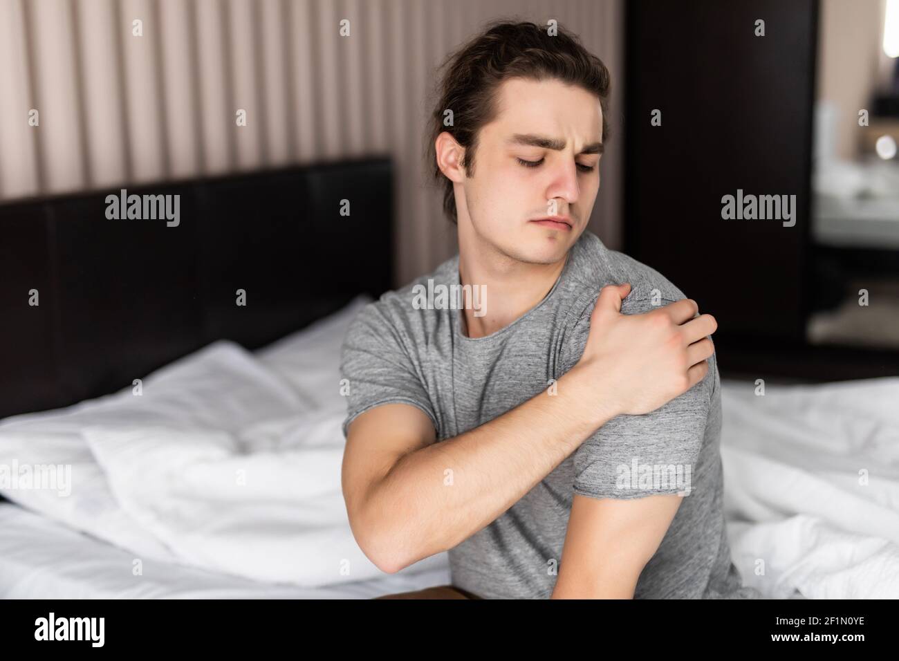 Man with upper arm pain.In the white bedroom there are boy. Guys are squeezing the upper arm. Stock Photo