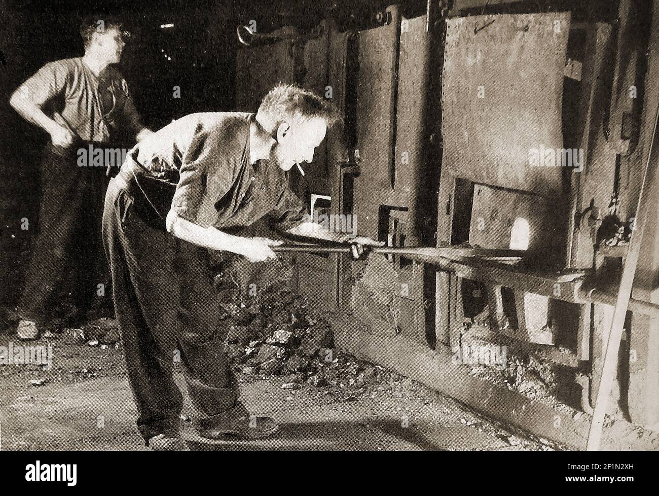 A circa 1930s image of a man puddling iron in a British iron foundry.  The procdess of Puddling is a step in the manufacture of high-grade iron using a crucible or furnace,   invented in Great Britain during the Industrial Revolution.   Bar iron  could be produced without without charcoal and replaced the earlier potting & stamping,charcoal use and  bloomery processes. Stock Photo