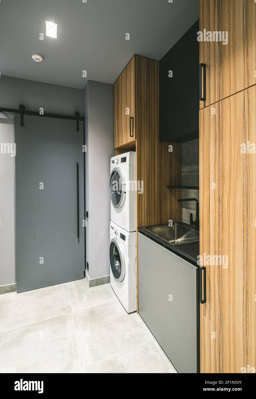 Modern interior of empty laundry room in luxury private house. Grey tones. Wooden cabinets. Washing machine. Stock Photo