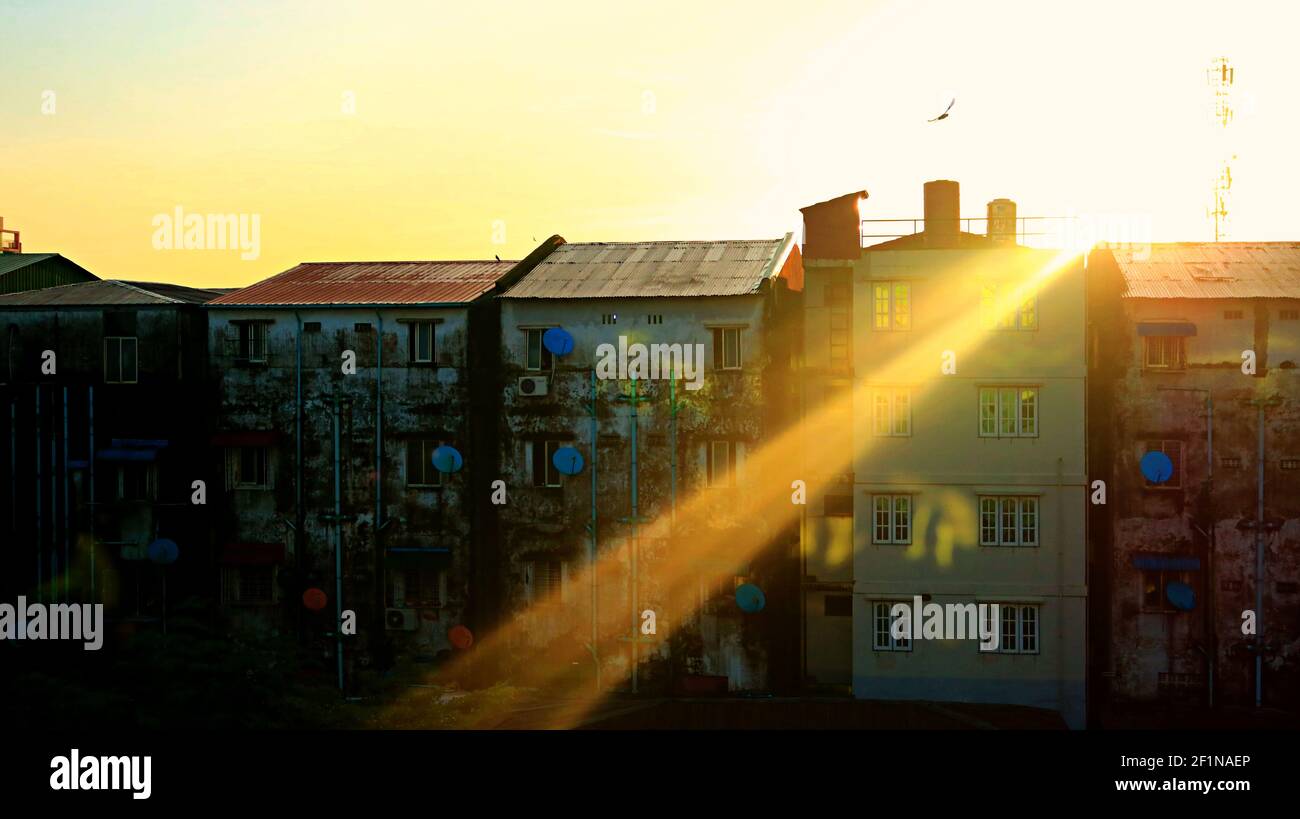 Good Morning Yangon: Sunbeam on rooftop of low rise buildings with a silhouette of a sole flying bird as the sun rises in the city capital of Myanmar Stock Photo