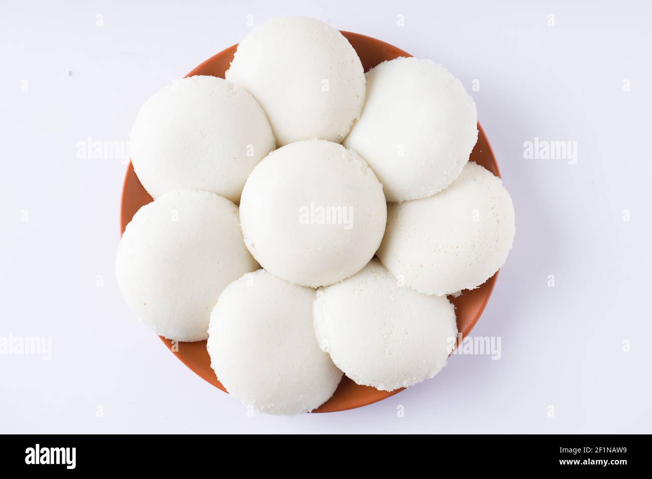 Idly or Idli, south indian main breakfast item which is beautifully arranged in an earthen ware with  white background. Stock Photo