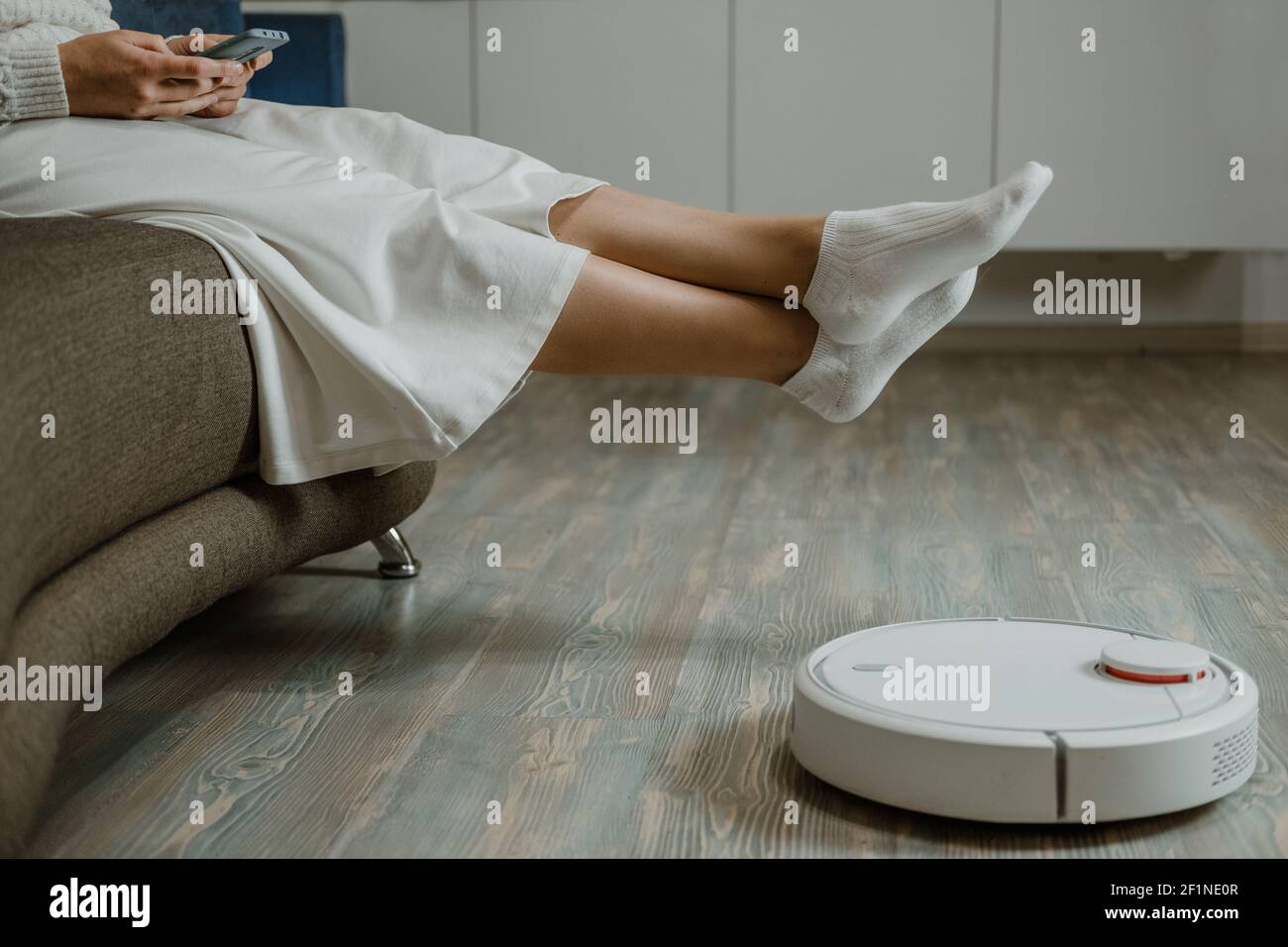 Woman Relaxing on sofa. Automatic robotic vacuum cleaner on laminate