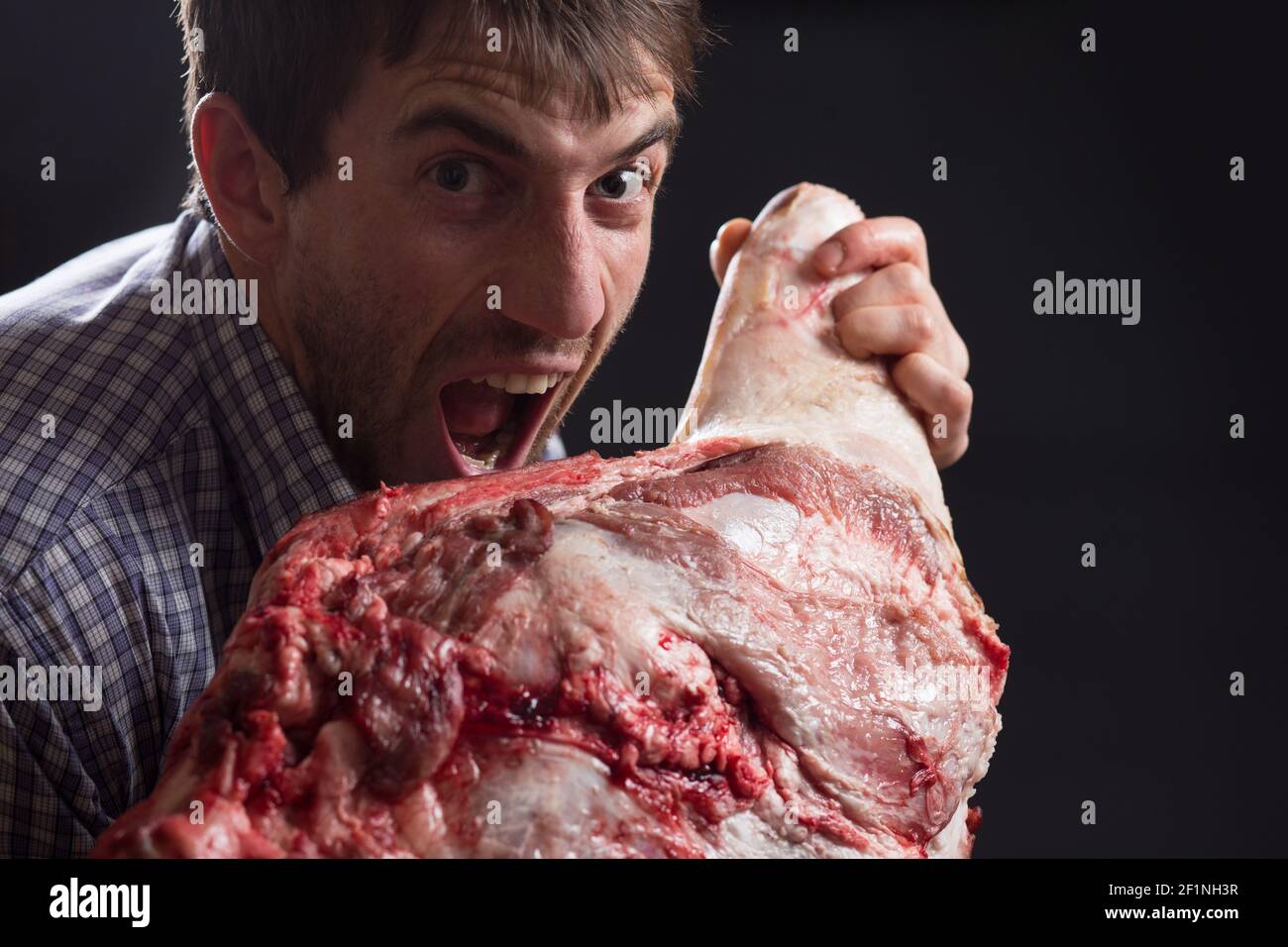 Crazy hungry man eating raw pork leg with crazy angry face. Stock Photo