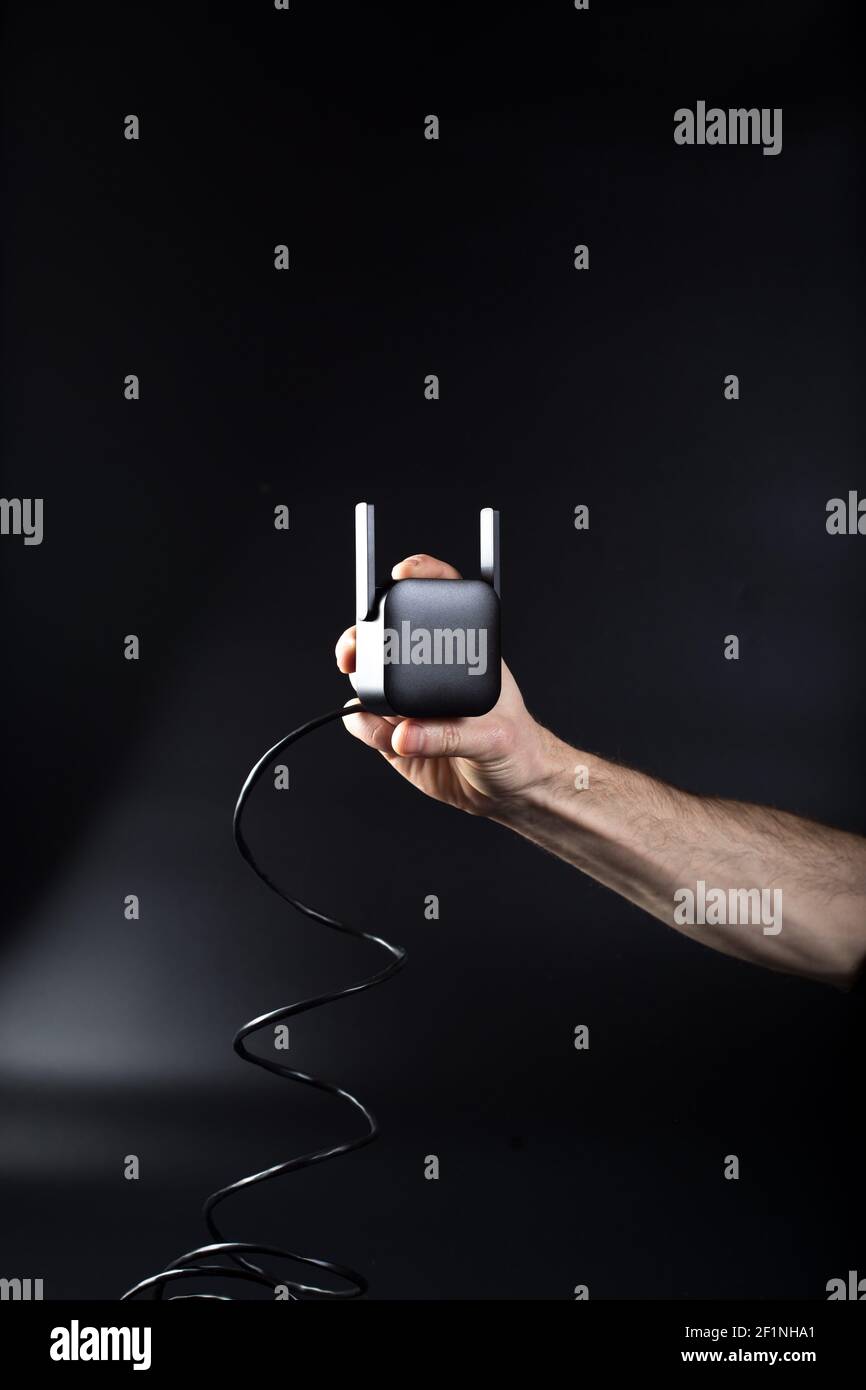 Hand holding black wifi router on black background with connected cable ...
