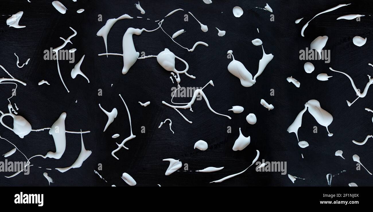 White splashes of wet fluide acrylic paint on a black texture gouache background. Long artistic banner Stock Photo