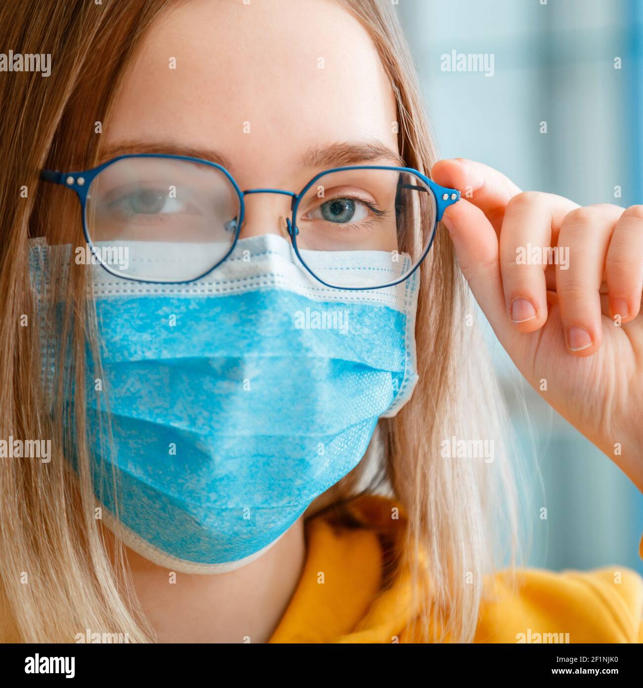 Foggy glasses wearing on young woman. close up portrait. Teenager girl in blue medical protective face mask and eyeglasses wipes blurred foggy misted Stock Photo