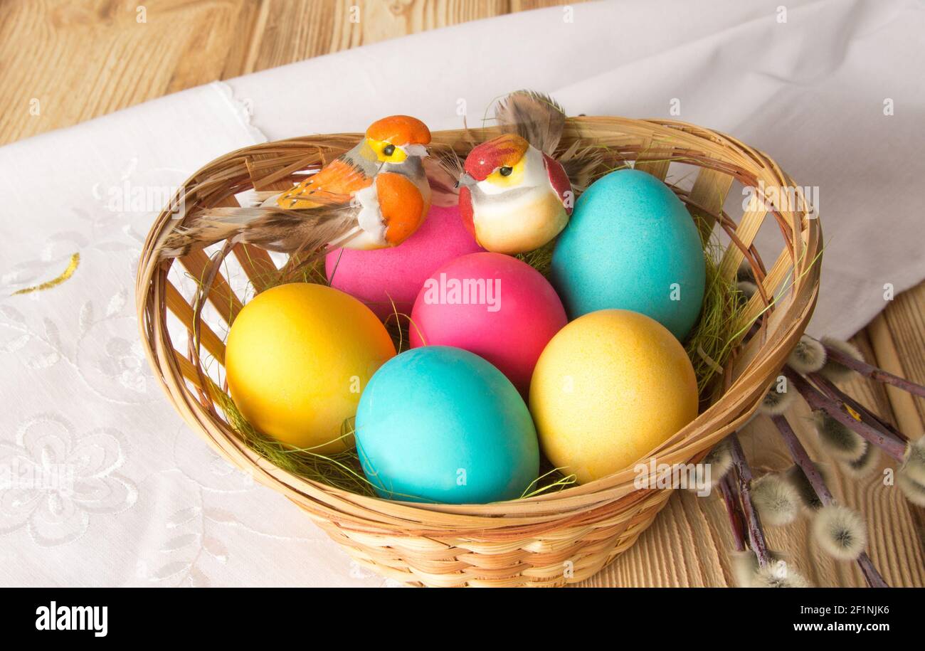 Two toy birds are hatching painted Easter eggs in a wicker plate. Stock Photo