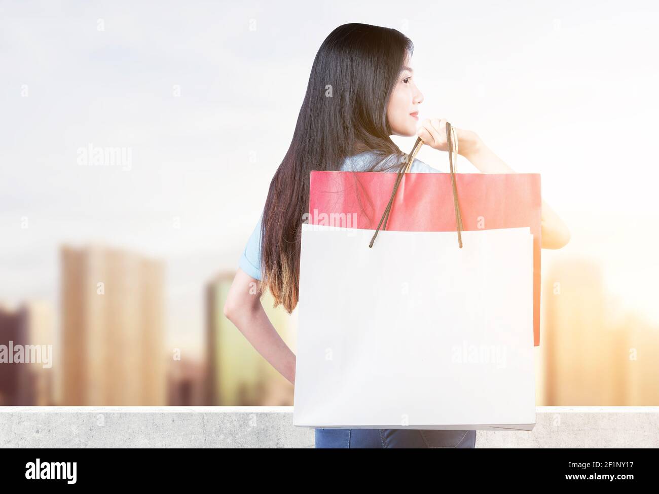 Rear view of Asian woman carrying shopping bags standing with cityscape ...