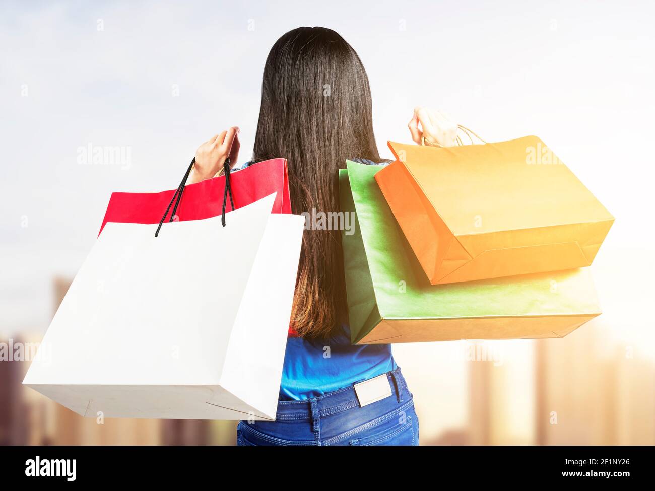 Rear view of Asian woman carrying shopping bags standing with cityscape ...