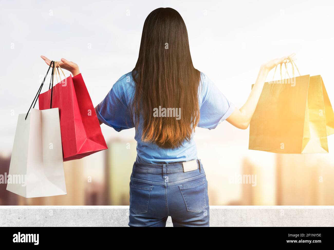 Rear view of Asian woman carrying shopping bags standing with cityscape ...