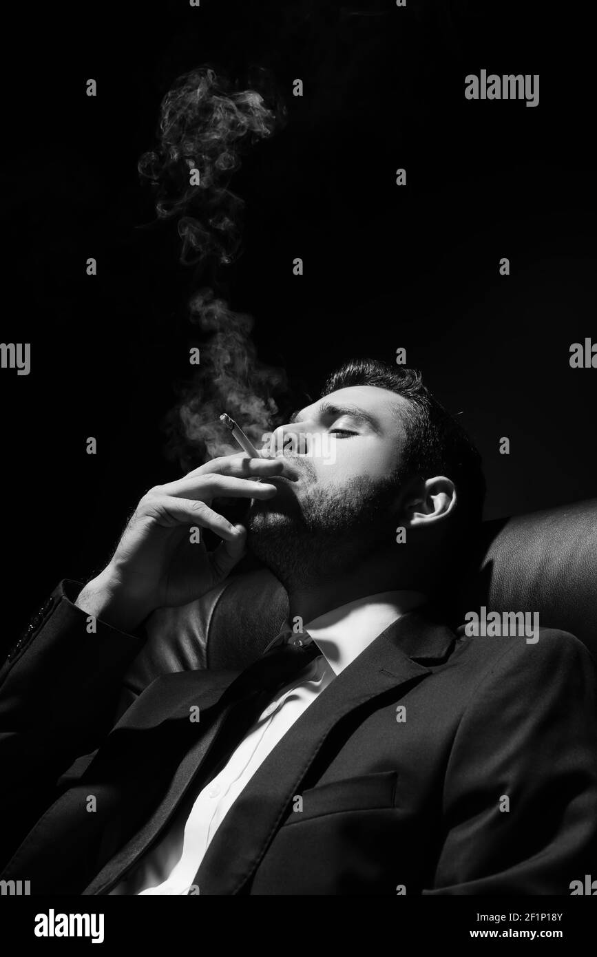 cigarette photography Monochrome shot of young man in suit smoking cigarette isolated on black  Stock Photo