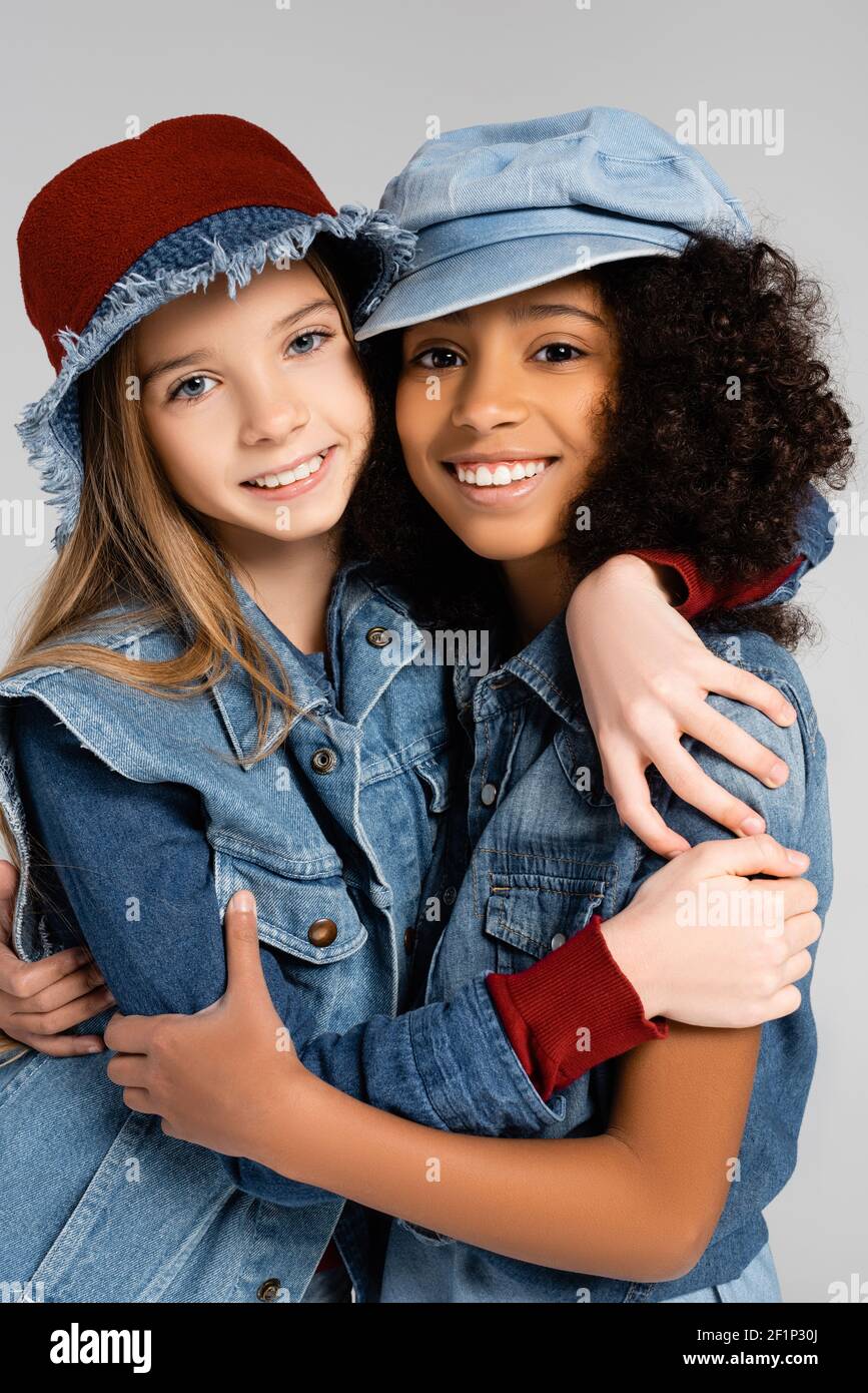 happy multicultural girls in stylish denim clothes hugging isolated on grey Stock Photo