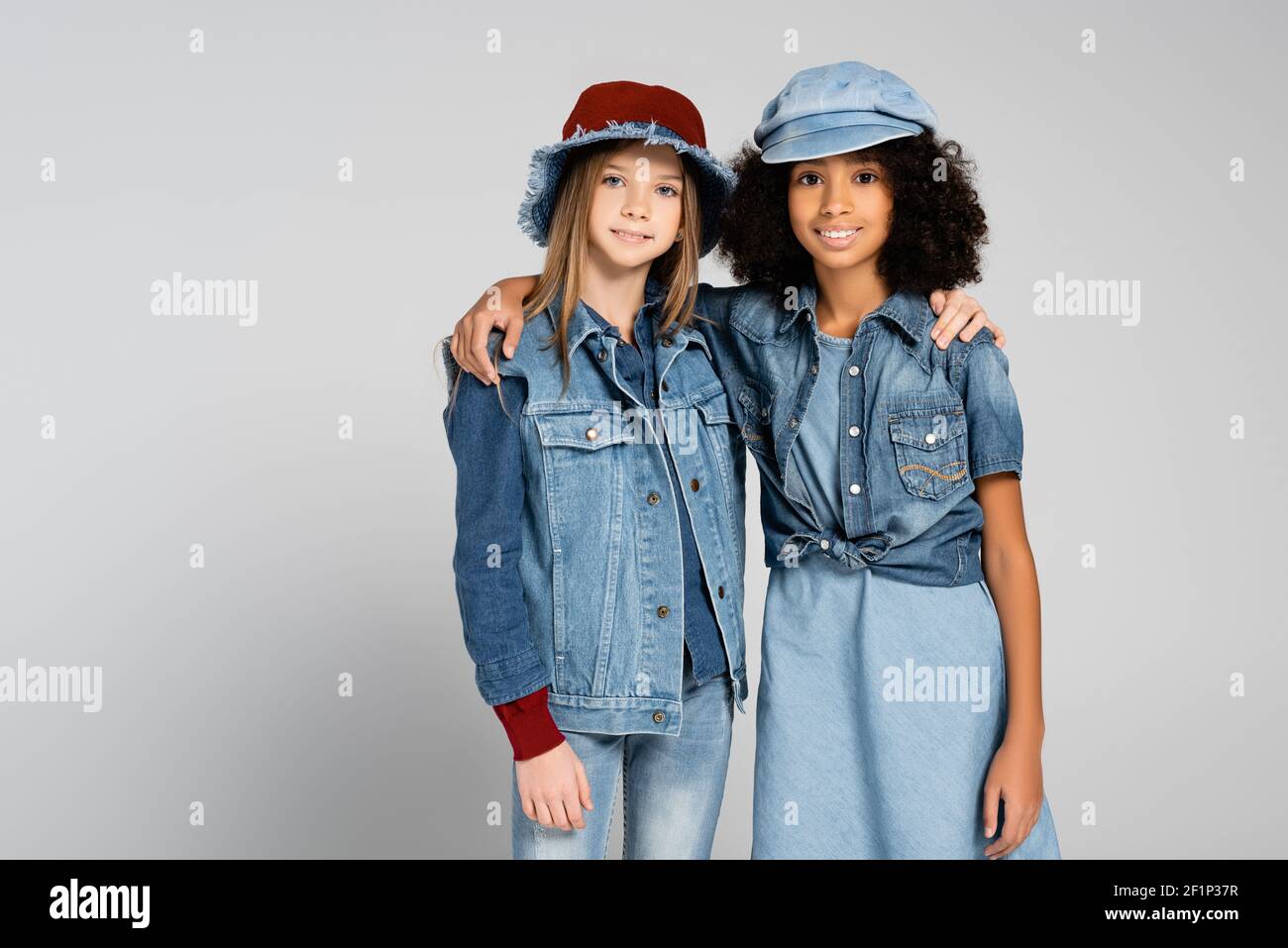 smiling multicultural kids in trendy denim clothes and hats hugging on grey Stock Photo