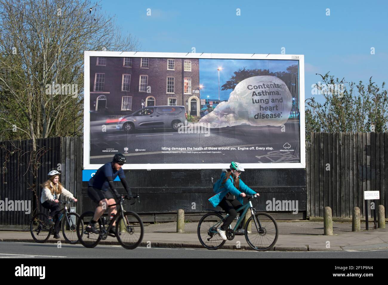 three cyclists pass a billboard warning of the pollution and threat to public health caused by engine idling, in twickenham, middlesex, england Stock Photo