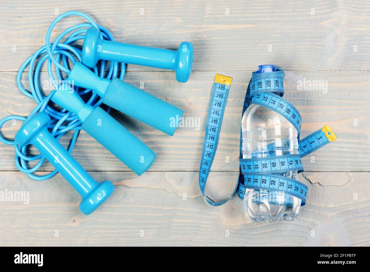 https://c8.alamy.com/comp/2F1PBTF/centimeter-in-cyan-blue-tied-around-bottle-on-wooden-vintage-background-tools-for-healthy-and-active-lifestyle-dumbbells-measuring-tape-and-jump-rope-top-view-workout-and-losing-weight-concept-2F1PBTF.jpg